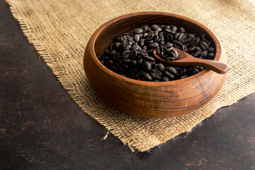 Fototapeta na wymiar Dark Roast Coffee Beans in a Wooden Bowl with Wooden Spoon and Burlap