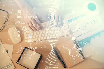Double exposure of man's hands typing over computer keyboard and DNA hologram drawing. Top view. Medical education concept.