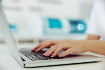 Closeup of laboratory assistant typing test results on laptop. Selective focus on hands.