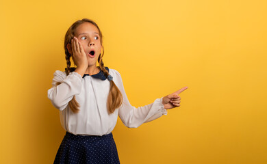 Young student is with shocked expression and indicates something. Yellow background