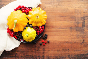 Fresh yellow squash and berries of viburnum and chokeberry on a round plate on a wooden brown board, top view, copy space. Autumn or Thanksgiving background.