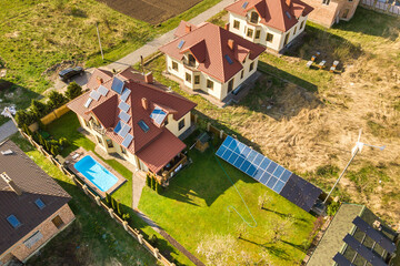 Fototapeta na wymiar Aerial view of a private house with green grass covered yard, solar panels on roof, swimming pool with blue water and wind turbine generator.