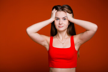 Fototapeta premium Young girl grabbing her head ruffling her hair due to piled up problems on an orange background