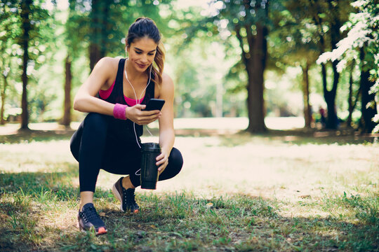 Young attractive caucasian female runner holding refreshment and resting from running.