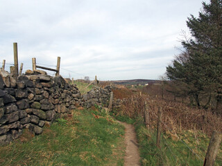 a narrow footpath between a dry stone wall and fence surrounding a meadow in west yorkshire countryside near heptonstall