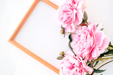 Wooden picture frame decorated with pink peony flower on white background.Copy space for text,top view,flat lay,selective focus
