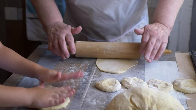 Funny blond boy helps beloved  grandmother in kitchen. elderly woman rolls pastry for pasties and puts minced meat. teenager touches dough. Kid and granny are happy together. shallow depth of field 