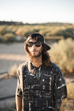 Modelo de estilo surfero con pelo largo, gafas de sol y gorra, en unas dunas de la playa