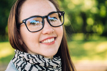 Caucasian girl of about thirty in glasses smiles and looks at the camera on a park background