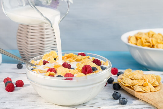 Pouring milk into a cup with cereal and fresh berries, close-up. Healthy summer breakfast. Healthy eating concept