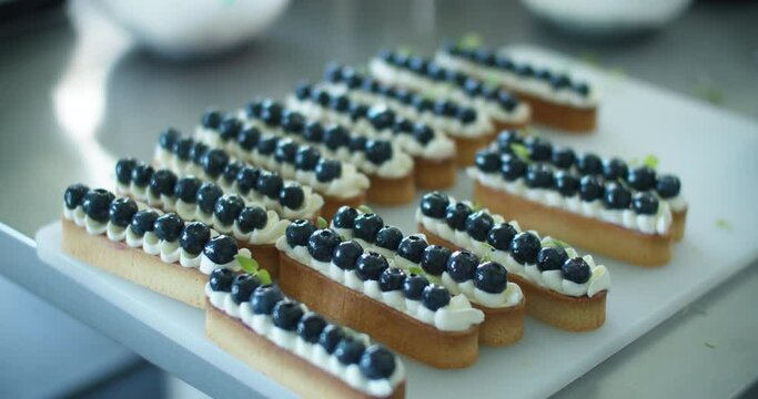 Women's hands decorate a cream dessert with blueberries on the kitchen table. Close up