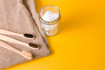 natural fabric, several different bamboo brushes and a glass jar of soda on a yellow background, copy space, eco friendly lifestyle concept