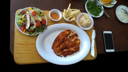 fish fillet with garlic mojo accompanied by salad rings, french fries sauce and condiments on a wooden board and even cost a cell phone