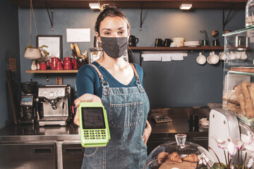 Caucasian woman offering card payment method in a small bakery business wearing mask durind covid-19 pandemic reopening after quarantine