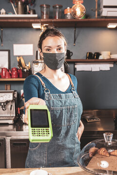 Caucasian woman offering card payment method in a small bakery business wearing mask durind covid-19 pandemic reopening after quarantine