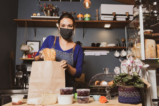 Caucasian woman packing bread for delivery in a small bakery business wearing mask durind covid-19 pandemic reopening after quarantine