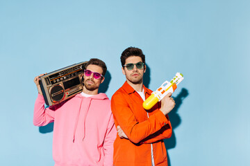 Man in pink hoodie and sunglasses holds record player. Guy on orange jacket and green eyeglasses...