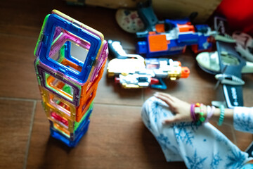 Little girl completing a tower with magnetic pieces inside her room.
