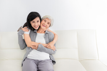 young Asian female hug old female in home, they feeling happy and smile, they sitting on sofa, mother's day, happiness family time