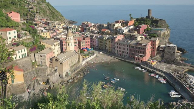 Vernazza,Liguria,Italy.June 2020. Beautiful view of the village: in the center the small port with its crystal clear sea,around the houses with colored facades.People walk in the square. Tilt movement