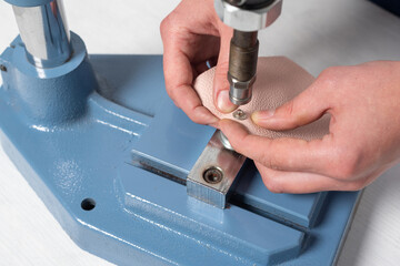 the hands of the master make holes for the buttons on a special installation press