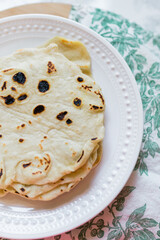 A white plate with homemade flour tortillas. Vertical photo. 