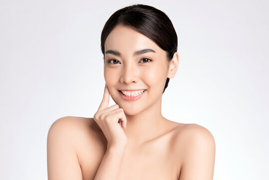 Beauty face. Smiling asian woman touching healthy skin portrait. Beautiful happy girl model with fresh glowing hydrated facial skin and natural makeup on white background