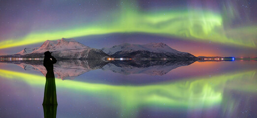 Young girl in dress and black hat walking on the water - Northern lights in the sky over Tromso,  Norway