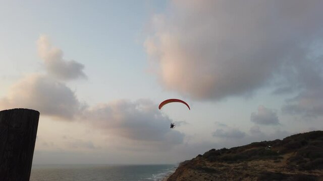 Motorized paraglider flying across the beach at sunset