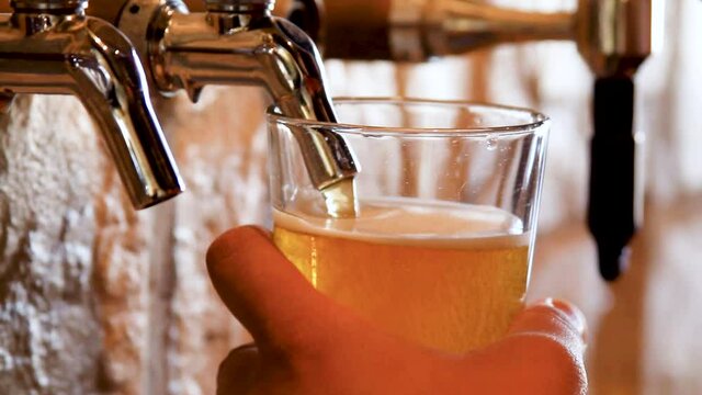 Close up shot of a tap pouring beer into a pint glass behind the bar.