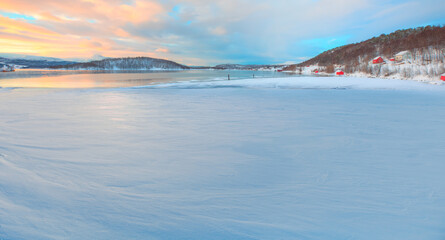 Fototapeta premium Panoramic view at fjord with coast of the Norwegian sea in the background snowy mountains at sunset - Snowy winter in the Arctic Circle - Tromso, Norway
