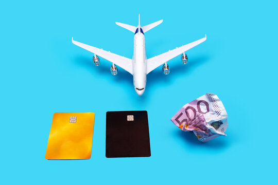 a plane, a crumpled bill, and a pair of plastic cards on a blue background. The photo symbolizes the lack of money for a ticket, flight, vacation, and the choice between cash and credit cards.