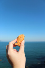 Hand holding a mini fish-shaped waffle with custard filling with the sea background in sunny day, South Korea