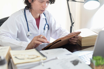Asian doctor researching reading medical books and online knowledge to find treatment patient guidelines In the doctor's room office