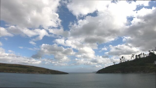 Time lapse passing white clouds over water surface and blue sky with land on both sides