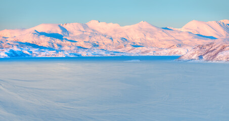 Obraz na płótnie Canvas Panoramic view at fjord with coast of the Norwegian sea in the background snowy mountains at sunset - Snowy winter in the Arctic Circle - Tromso, Norway