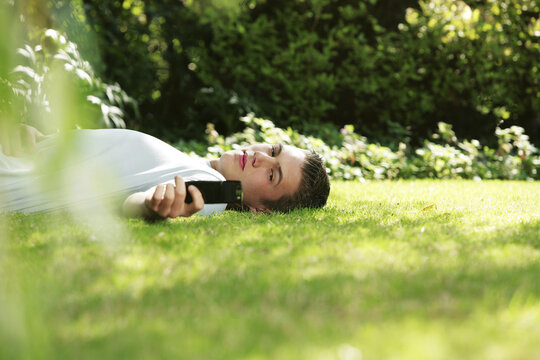 Young man lying on the grass, holding a cellular phone