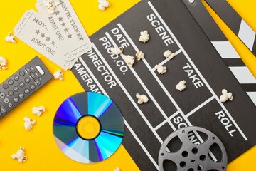 ovie clapper or clapper-board with dvd movie disc, film reel, popcorn, remote control and movie theatre tickets flat lay top view from above on orange - home cinema or movie night concept