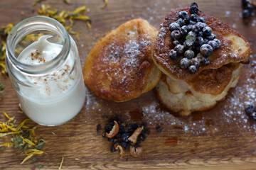 Fritters with fresh blueberries in icing sugar on a wooden table. Dried chamomile and apple.