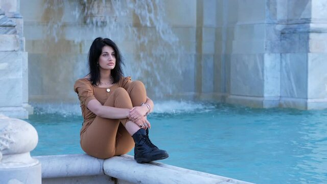 depressed pensive woman sitting on the wall of janiculum fountain.