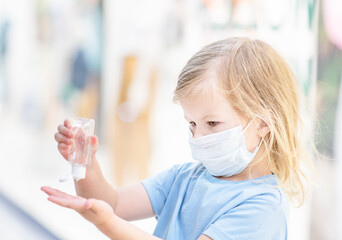 Little girl wearing medical protective mask during coronavirus and flu outbreak applies sanitizer for cleaning hands in a public crowded place - in a shopping mall or airport