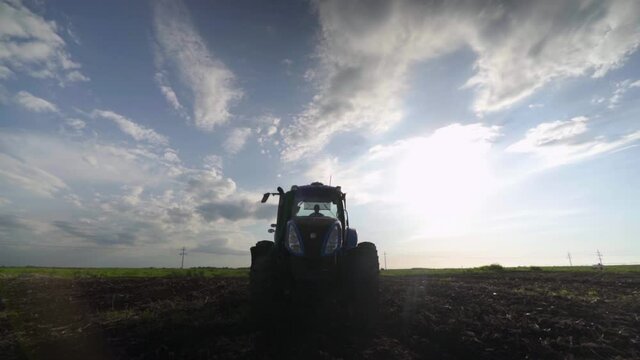 Blue tractor on a field comes closer to camera. clowds in the sky