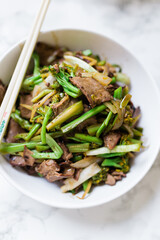 A delicious bowl with stir-fried beef and broccoli in a round white porcelain bowl with chopsticks resting on the bowl. Vertical photo.