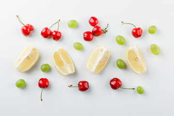 Naklejka na ściany i meble Grape grains with lemon slices, cherries on white background, flat lay.