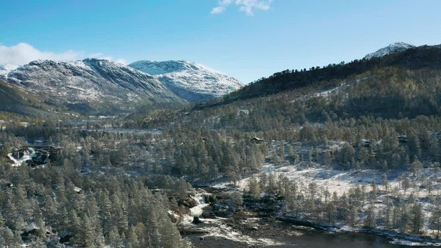 Aerial view of the vast valley of the Gaula river. The river is meandering through the valley, flowing to the waterfalls. Dense pine forest covering the valley's floor. Fresh snow is on the ground.