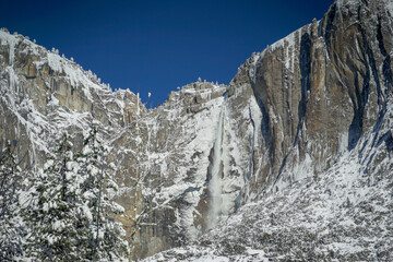 Wonderful waterfall and Half Dome at Yosemite Valley in the winter with white snow covering the...