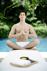 A guy doing yoga by the poolside