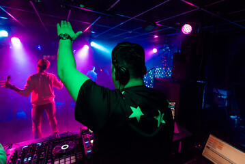 back of a male DJ with a raised hand in headphones at an electronic concert