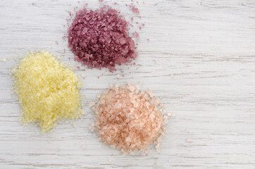 Piles of pink, yellow and red natural mineral sea aroma bath salts on wooden background, Spa and body care, with copy space