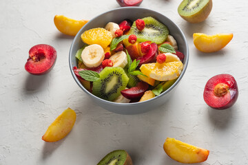 Concept of low calories delicious desserts. Summer fresh bowl with colorful fruit salad. Healthy natural organic food. Tasty sweet snack. Grey background. 